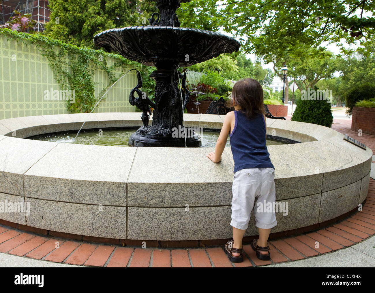 Kleines Kind lehnt sich an einen Brunnen, einen besseren Blick zu bekommen Stockfoto