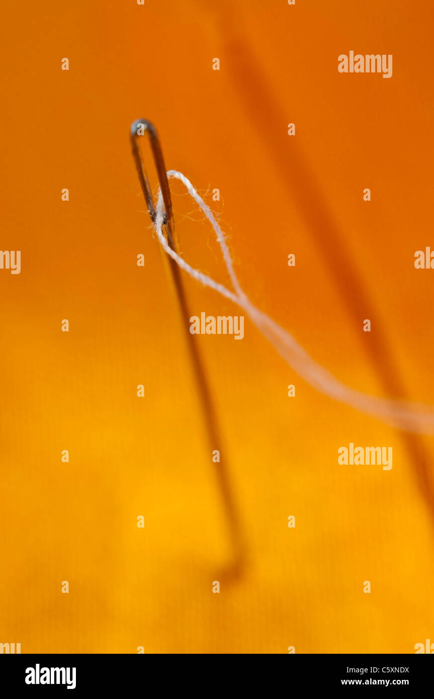 Nadel mit weißem Faden auf orange Seide Stockfoto