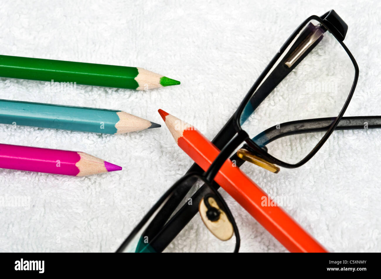 Bleistifte und Brillen auf weißem Stoff Stockfoto