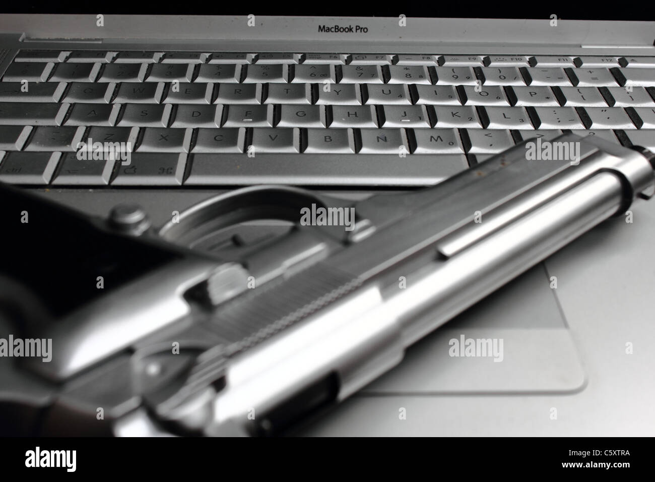 eine silberne Pistole auf einem Macbook pro Laptop, Konzeptbild, Metapher Stockfoto