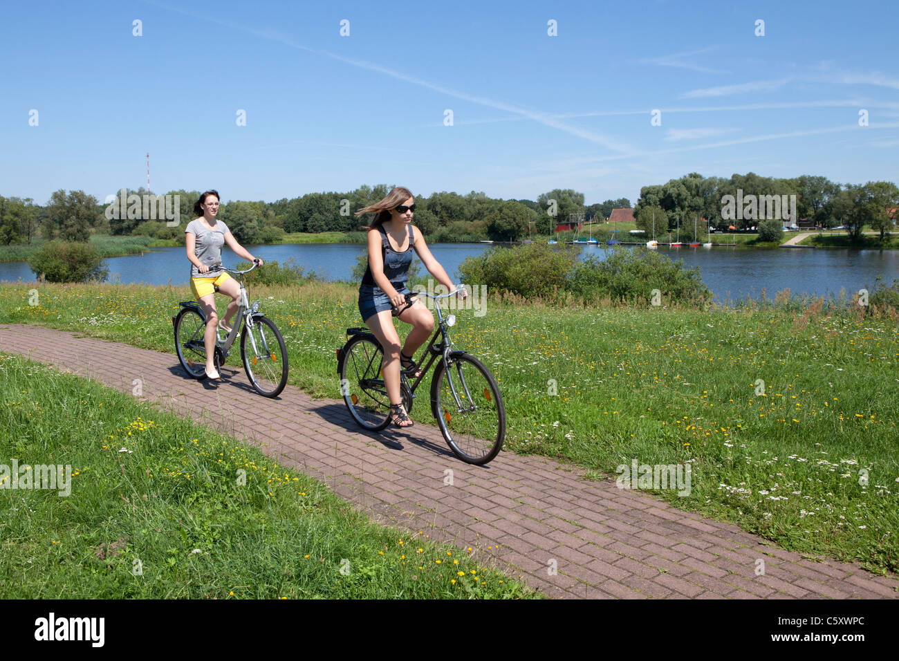 zwei Mädchen, Radfahren auf dem Deich neben See Gartow, Nature Reserve Elbufer-Drawehn, Niedersachsen Stockfoto