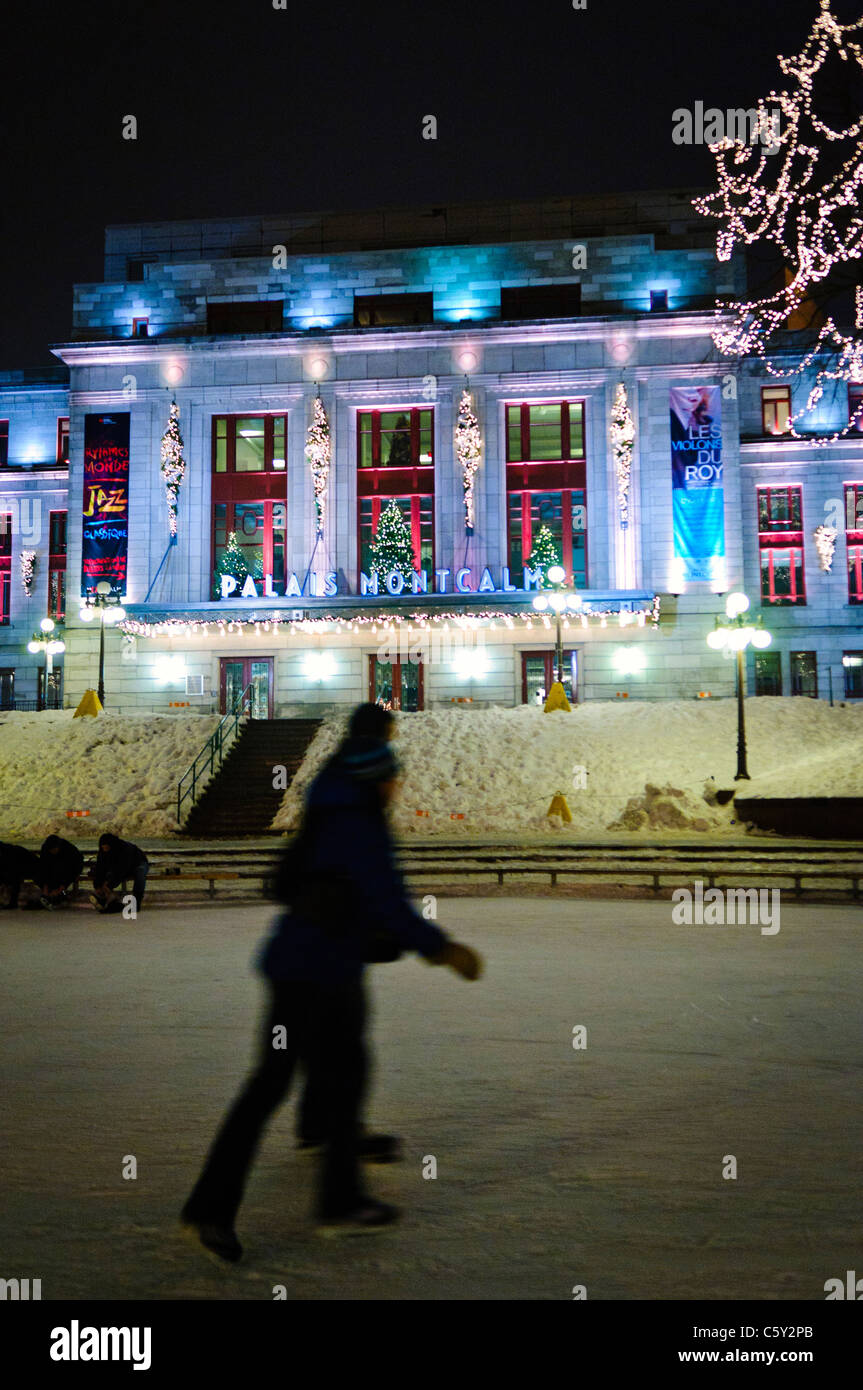 QUEBEC CITY, Kanada – Eisläufer gleiten über eine Eisbahn vor dem eleganten Palais Montcalm. Die beleuchtete Fassade des historischen Gebäudes bietet eine atemberaubende Kulisse für Wintererholung im Herzen des Kulturviertels von Quebec City. Stockfoto