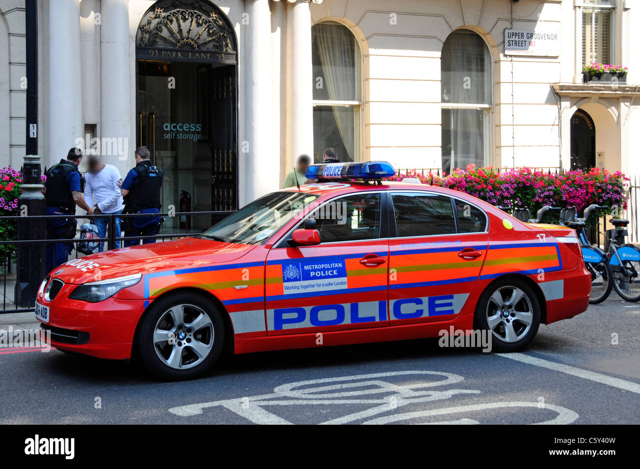 Londoner Straßenszene Metropolitan Polizisten bei der Arbeit suchen zwei Personen auf dem Bürgersteig (verdeckte Gesichter) Neben Polizeiauto Mayfair London England Großbritannien Stockfoto