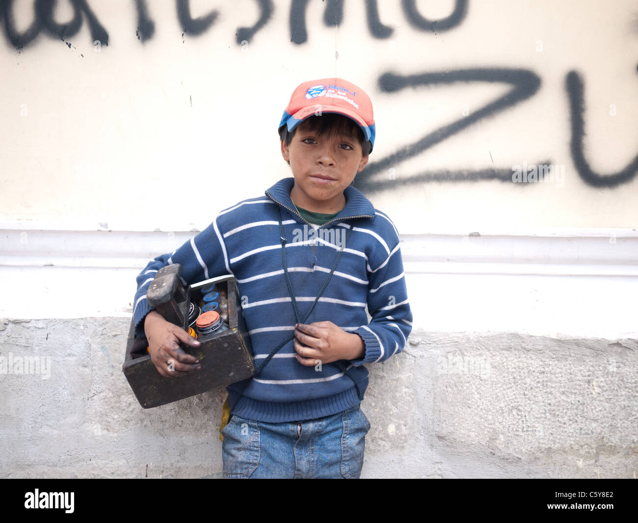 Ein Schuh Glanz junge steht an einer Graffiti besprühten Wand in Quito, Ecuador. Stockfoto