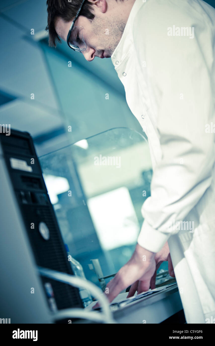 junge männliche Wissenschaftler tragen Brillen und weißen Laborkittel im Wissenschaftslabor hält Zwischenablage durch computer Stockfoto