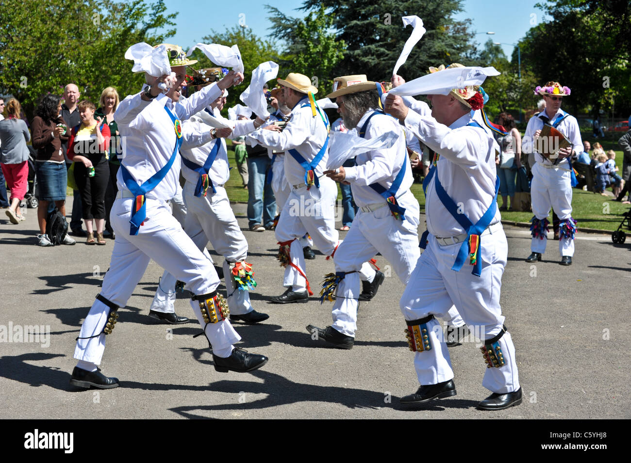 Eine Gruppe von traditionellen englischen Morris Dancers winken Taschentücher in der Luft, beobachtet von einer Menschenmenge in einem Park an einem sonnigen Mai-Tag Stockfoto