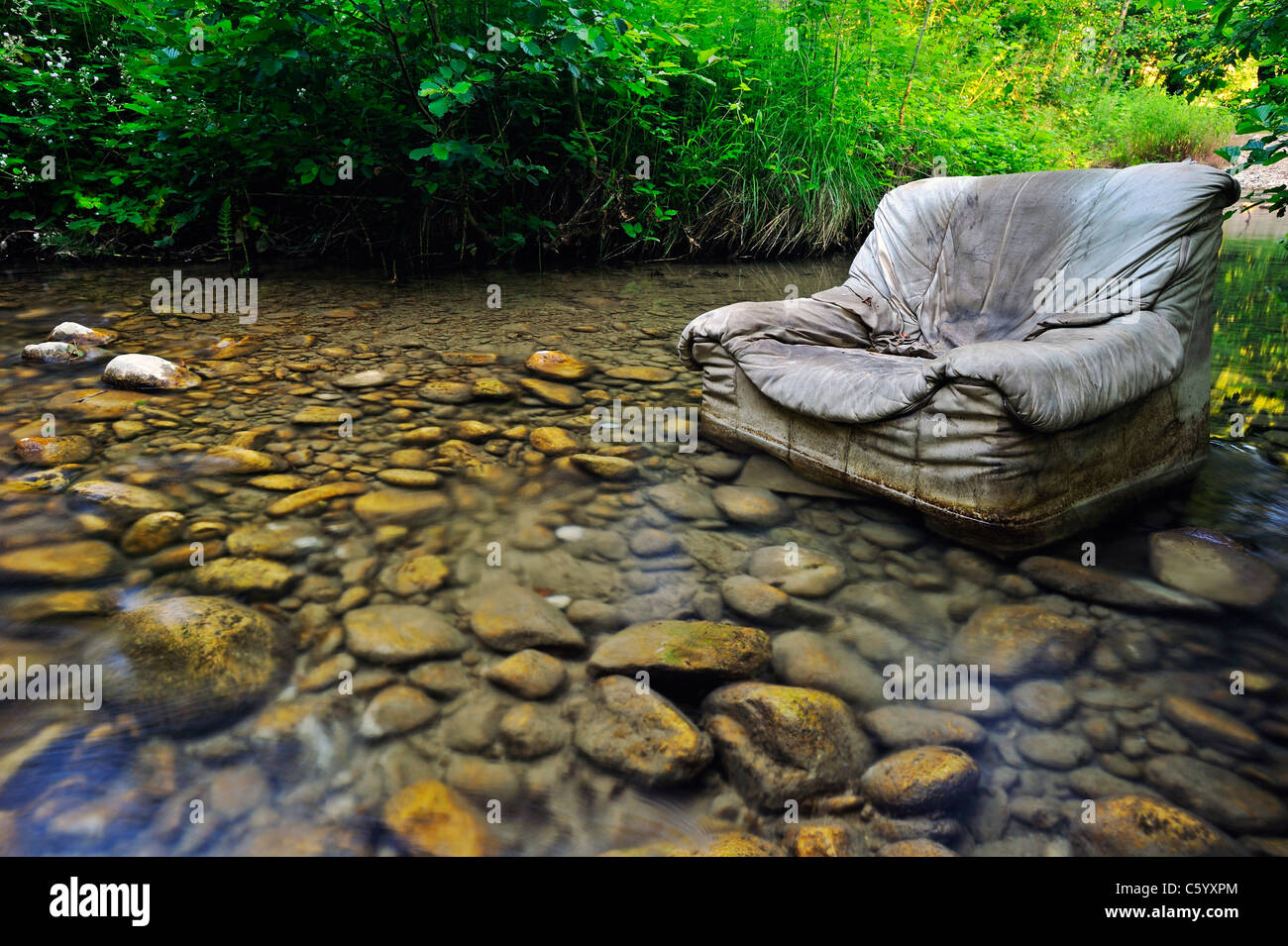 Fliegen Sie kippen. Ein alten Sessel entsorgt illegal in klaren Waldbach. Stockfoto