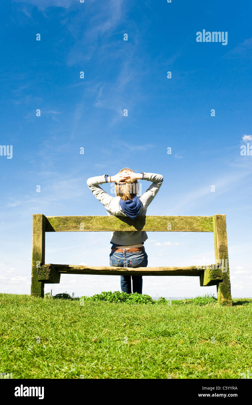 Entspannen Sie sich auf einer Parkbank an einem klaren Sommertag junge Frau Stockfoto