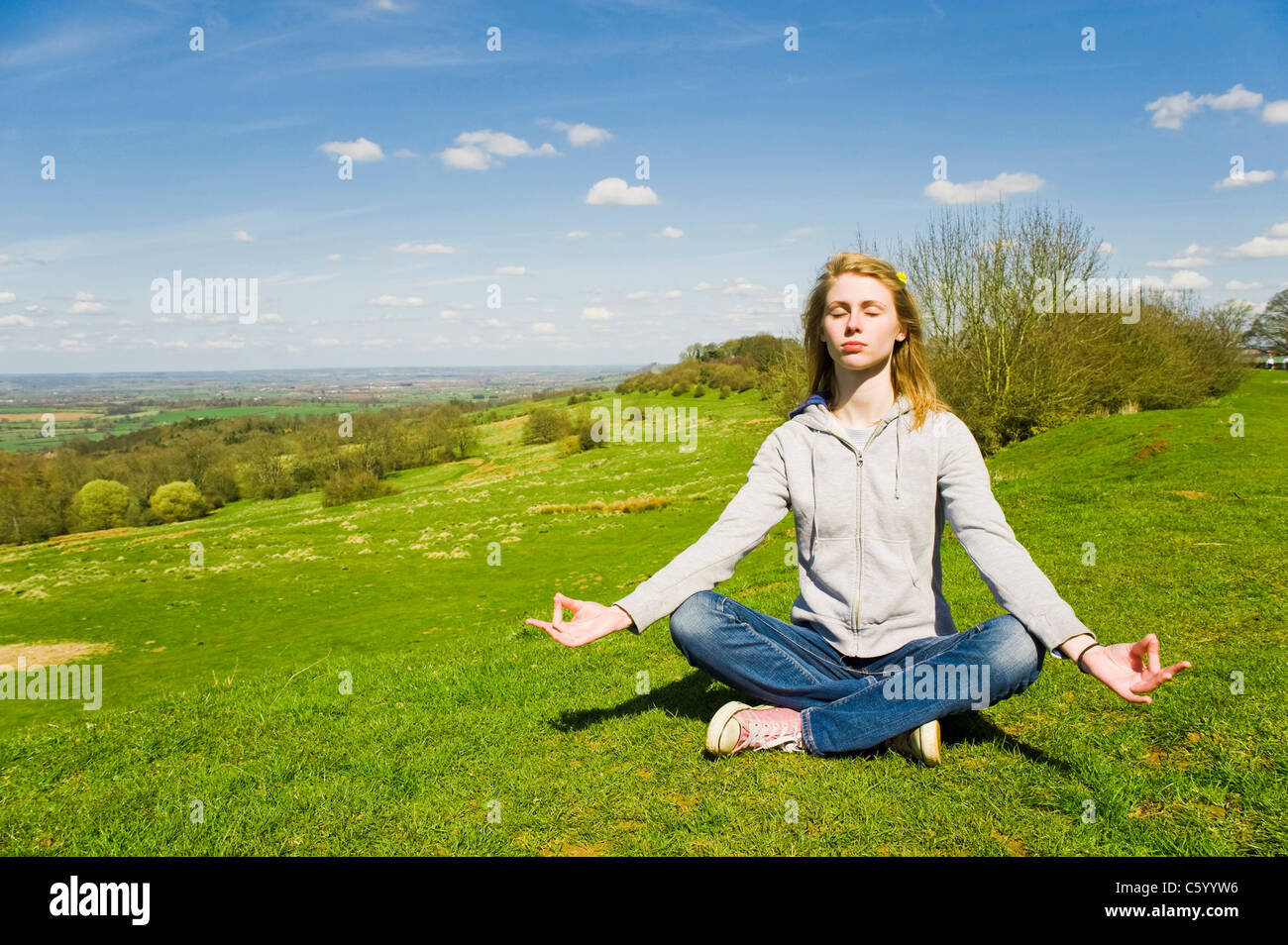 Kaukasische Mädchen meditieren im Freien vor einem strahlend blauen Himmel und grüne Landschaft Stockfoto