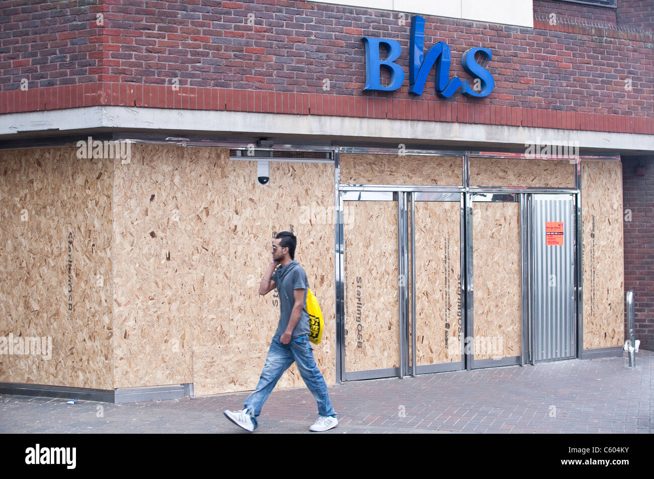 Ein Mann geht BHS auf Walthamstow High Street, nach den Unruhen von London auf 8. August 2011 mit Brettern vernagelt. Stockfoto