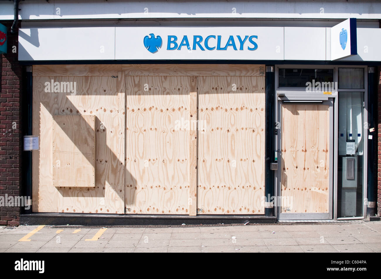 Ein Mann geht über Barclays Bank auf Walthamstow High Street, nach den Unruhen von London auf 8. August 2011 mit Brettern vernagelt. Stockfoto