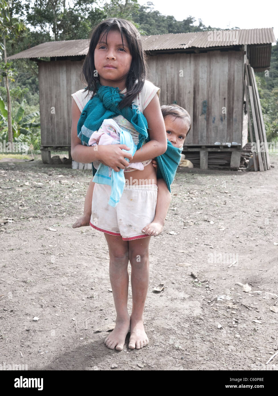 Ein junges Mädchen trägt ihren jüngeren Bruder auf dem Rücken vor ihrem Haus in den Amazonas-Dschungel. Stockfoto