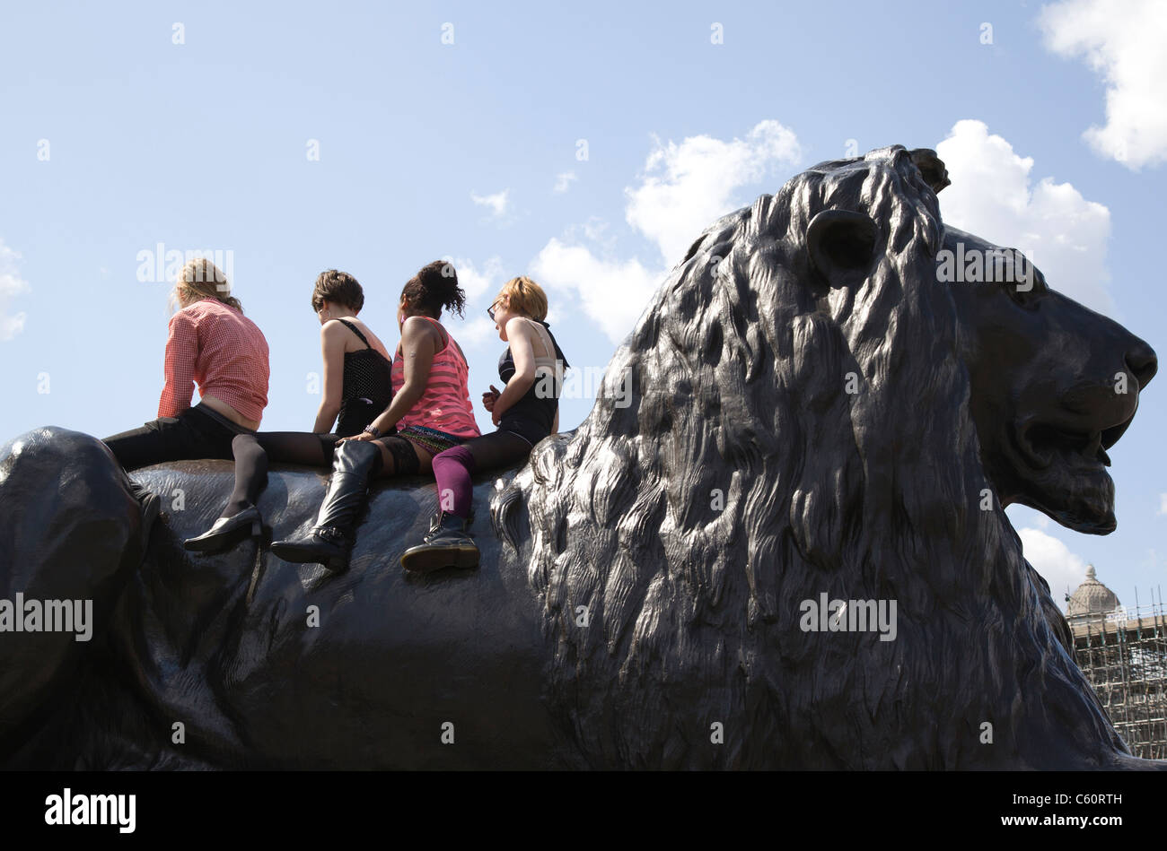 Vier anonyme Kinder sitzen auf der Rückseite eine Löwenstatue am Londoner Trafalgar Square Stockfoto