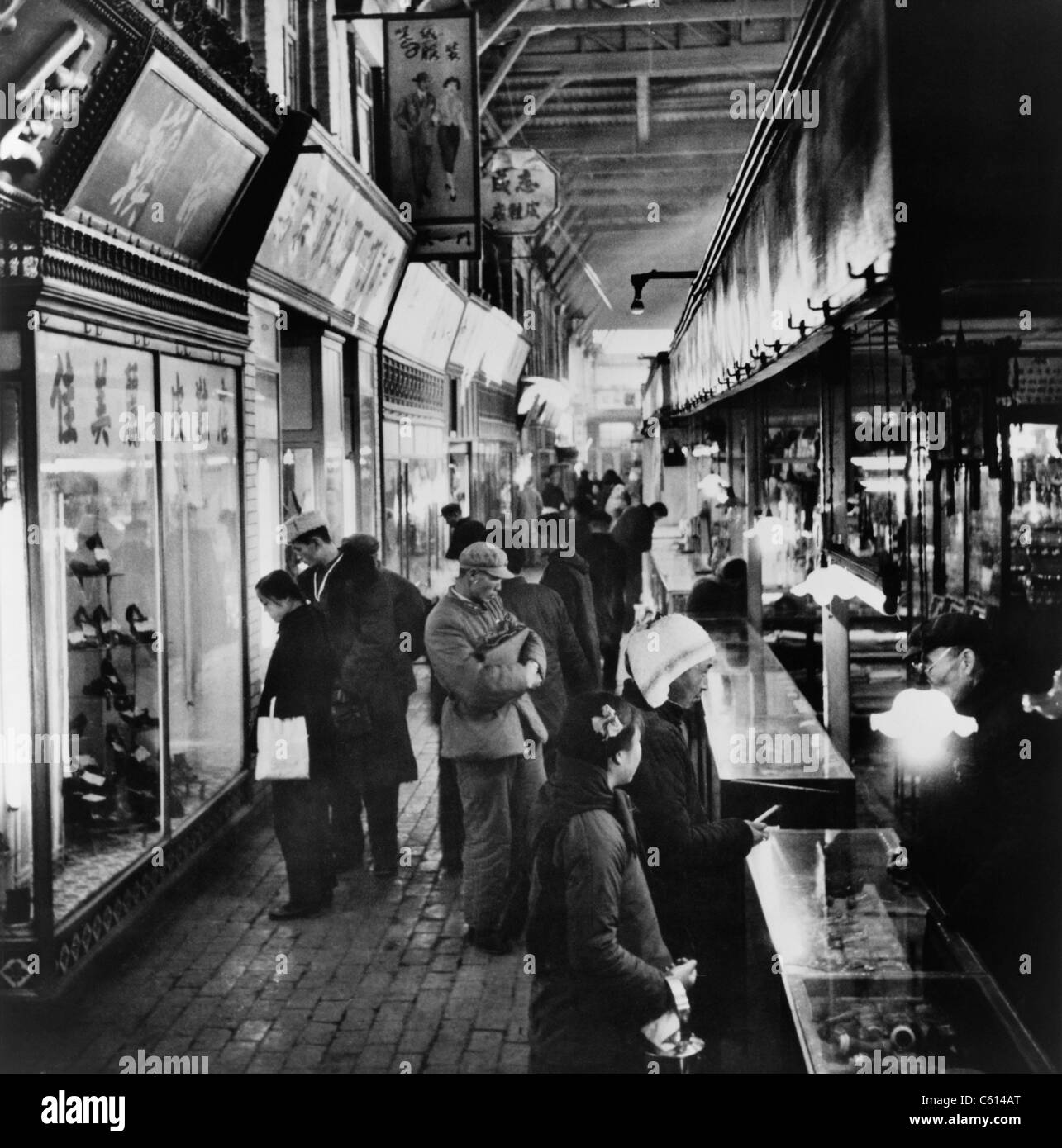Chinesische Käufer eye Konsumgüter an Schaltern und Schaufenster auf dem Tung ein Basar in Peking. 1964. (BSLOC_2010_18_100) Stockfoto