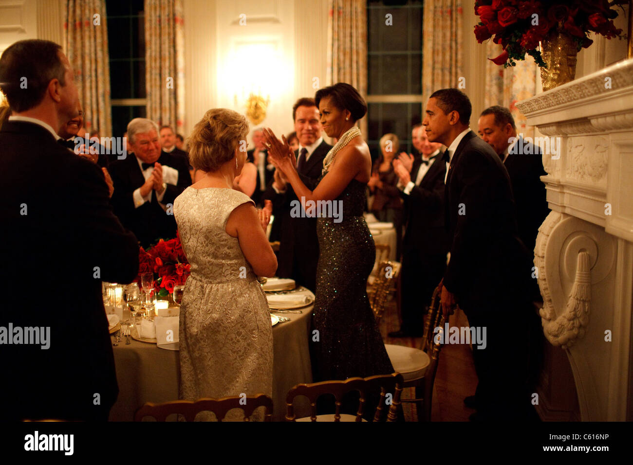 Präsident Obama zieht sich der Stuhl für Michelle Obama im Weißen Haus Governors Ball. Kaliforniens Gouverneur Arnold Schwarzenegger ist neben Michelle, die eine tiefe purpurrote Pailletten trägerlosen Kleid von Peter Soronen mit einem Multi-gestrandete Kette aus Perlen und Kristallen von Tom Binns trägt. 22. Februar 2009., Foto: Everett Collection(BSLOC 2011 7 136) Stockfoto