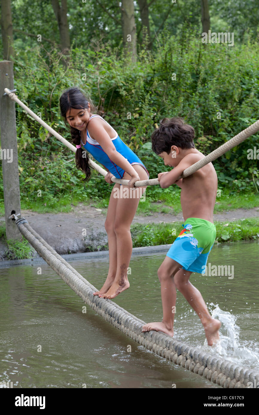 Kinder bekleidet schwimmen Anzüge balancieren auf einem Seil über dem Wasser Stockfoto