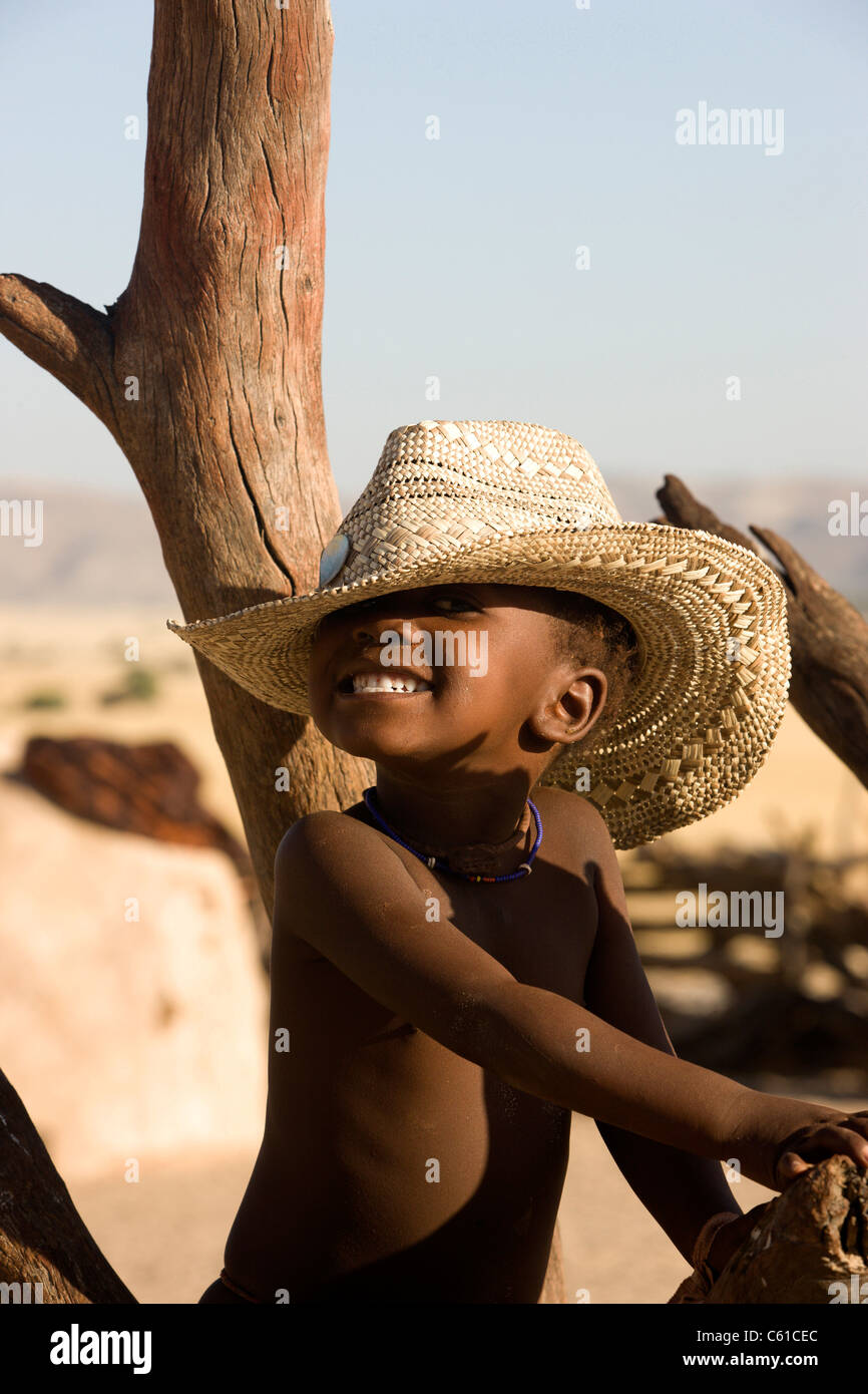 Ein fröhlicher kleiner Himba junge lächelt während sportlichen Westernstil Hut. Purros, nördlichen Kaokoland, Kaokoveld, Namibia. Stockfoto