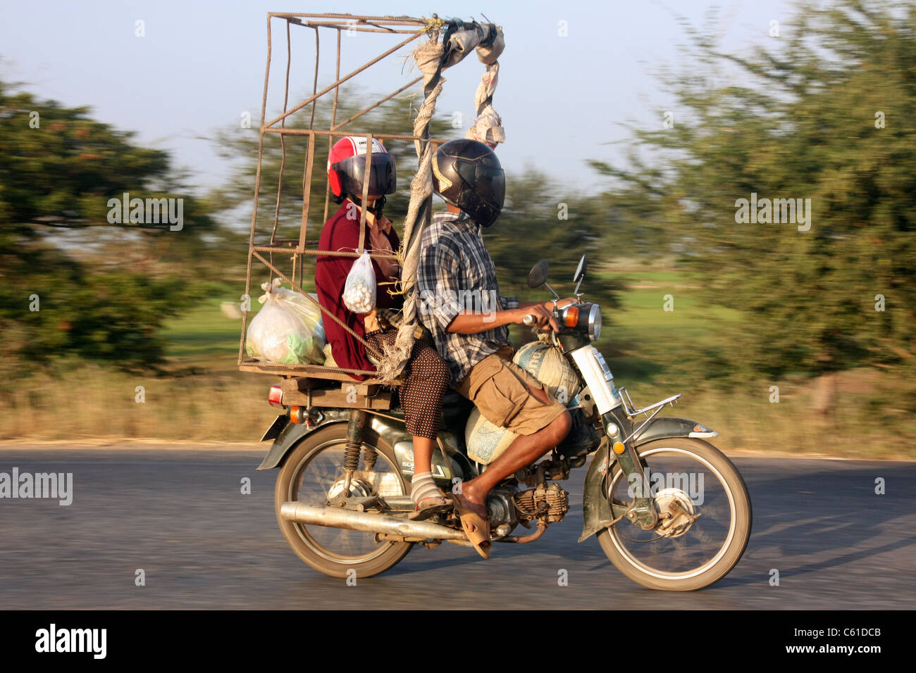Moped Fahrer trägt Frau Passagier- und eine instabile Eisenrahmen aus dem Markt durch ländlichen Kambodscha Stockfoto