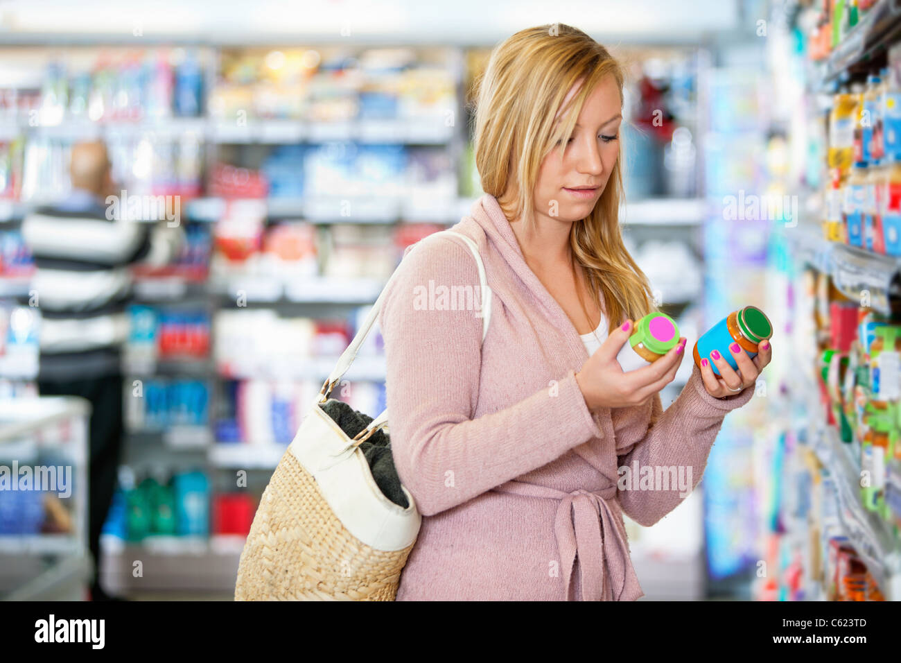 Junge Frau mit Glas im Supermarkt mit Menschen im Hintergrund Stockfoto