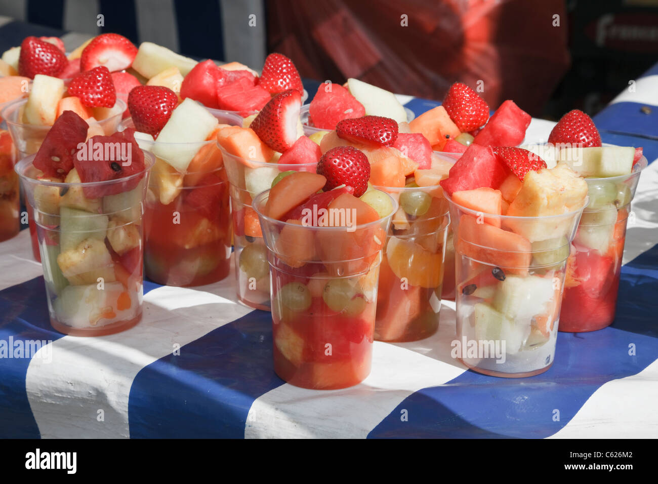 Gemischte frische Fruchtcocktails zum Verkauf in Einweg-Plastikbecher auf einem Marktstand mit blauen und weißen Tischdecke im Sommer Stockfoto