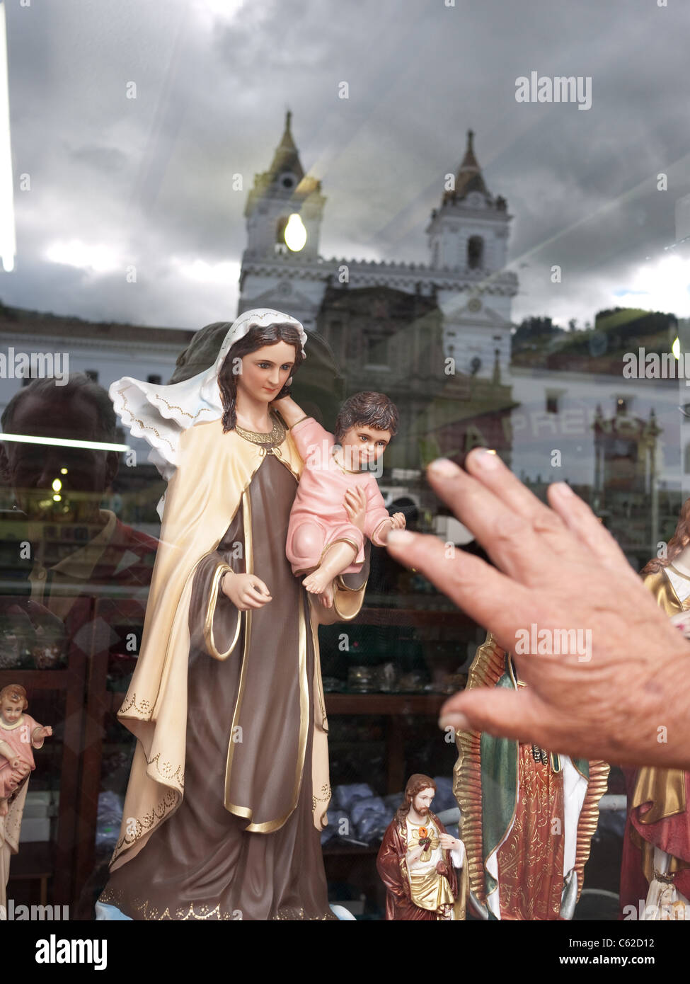 Hand greift eine Marienstatue mit Kirche im Hintergrund zu berühren. Stockfoto