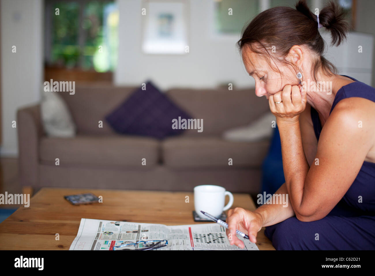 Frau 40er Entspannung zu Hause mit Kreuzworträtsel und Becher Tee Stockfoto
