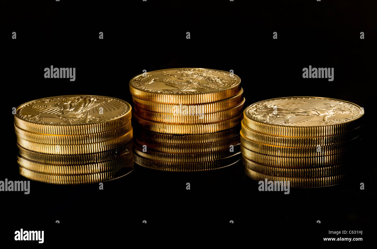 Nahaufnahme einer solid gold Eagle 1 Unze Münze auf anderen Münzen gestapelt und spiegelt sich in schwarze Oberfläche Stockfoto