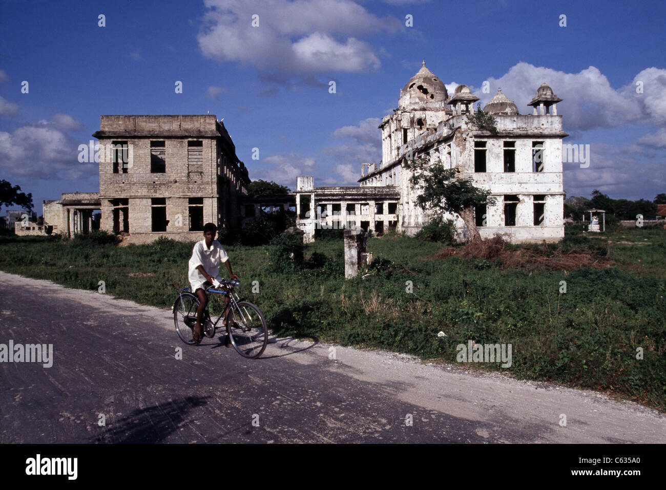 Ein Tamil Boy Fahrrad vorbei an zerstörten Regierungsgebäude in Jaffna, Sri Lanka. Stockfoto