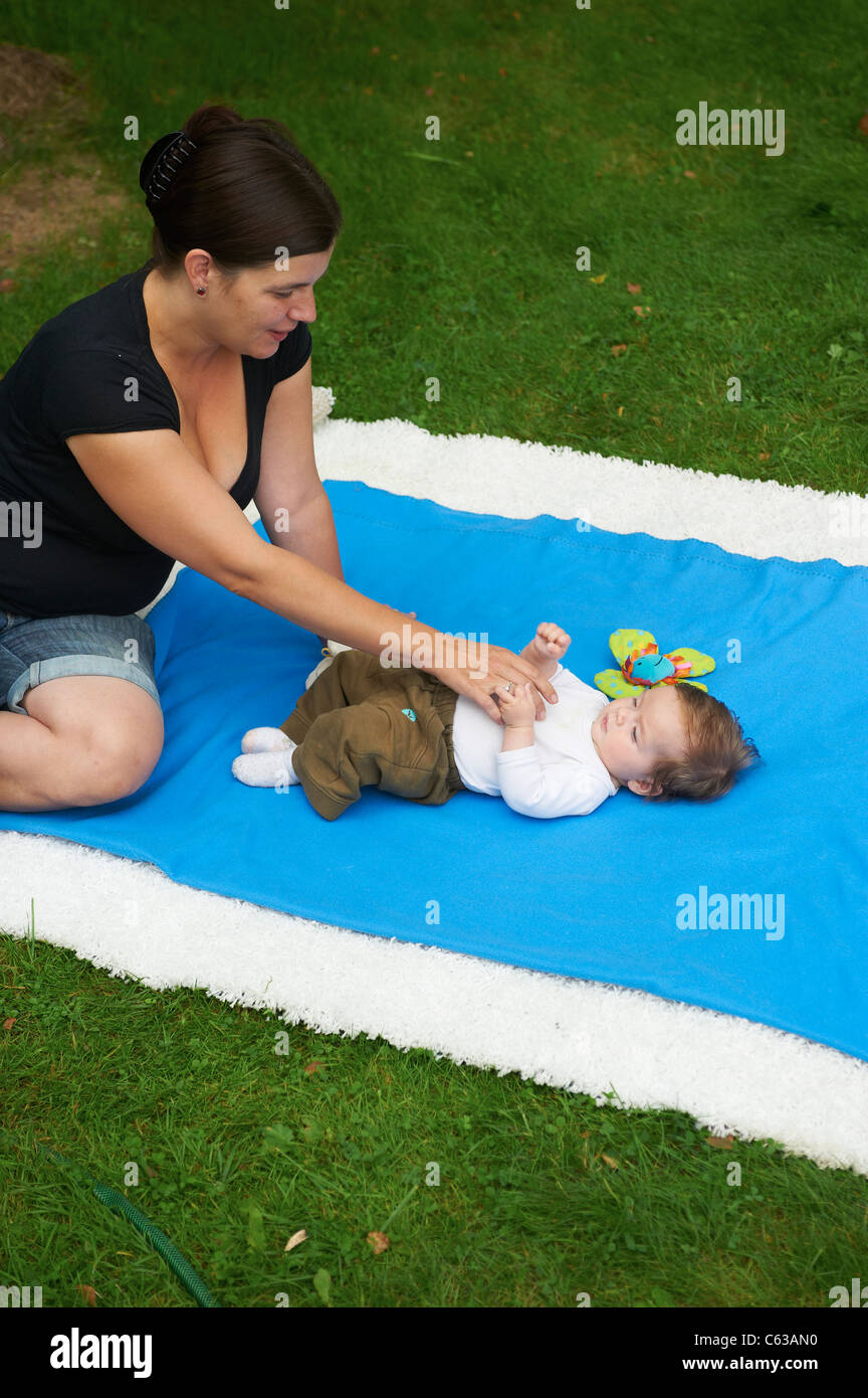 kleines Kind Mädchen auf blaue Decke liegend mit Mutter im grünen Rasen außerhalb Stockfoto