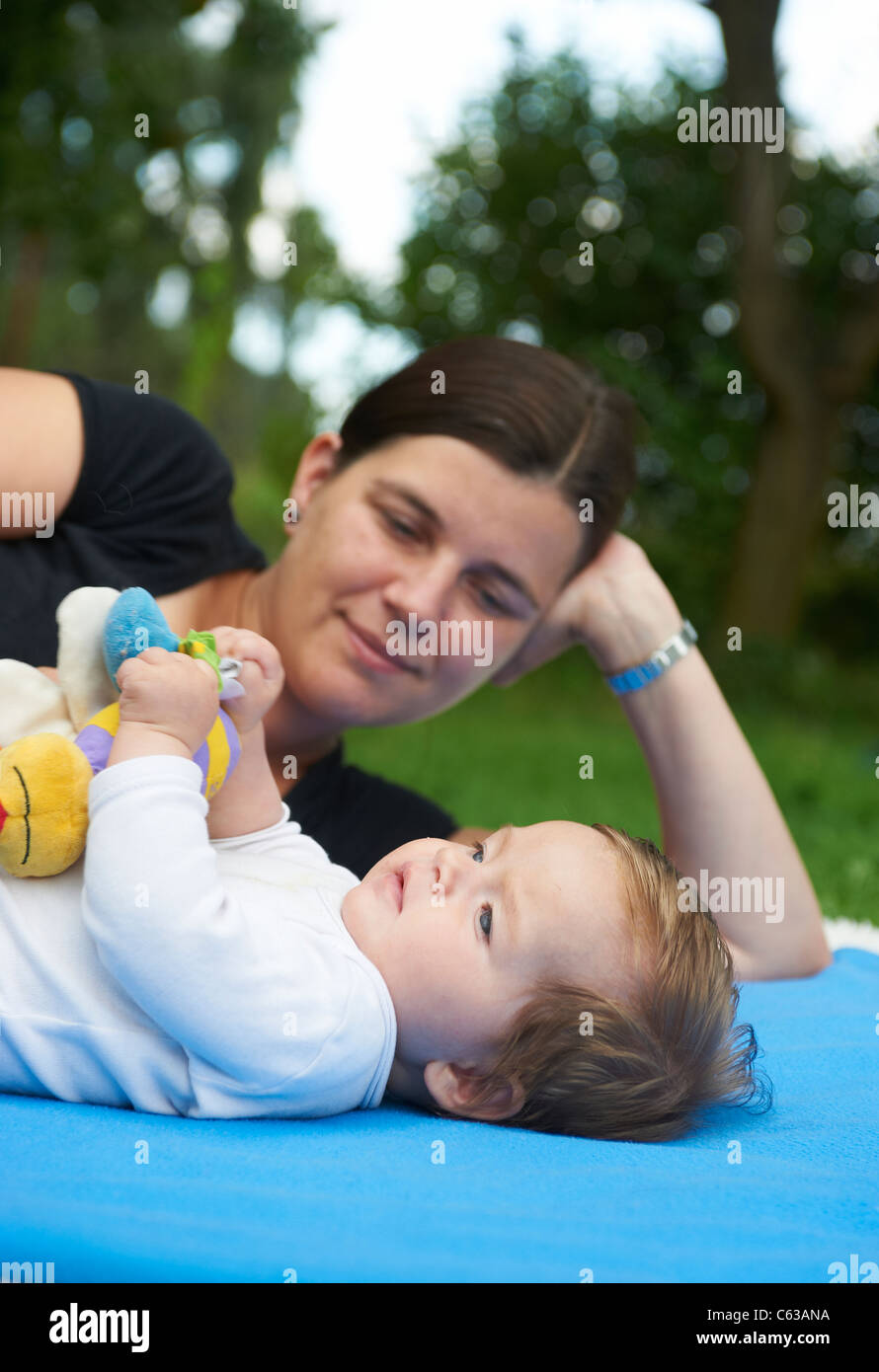 kleines Kind Mädchen auf blaue Decke liegend mit Mutter im grünen Rasen außerhalb Stockfoto