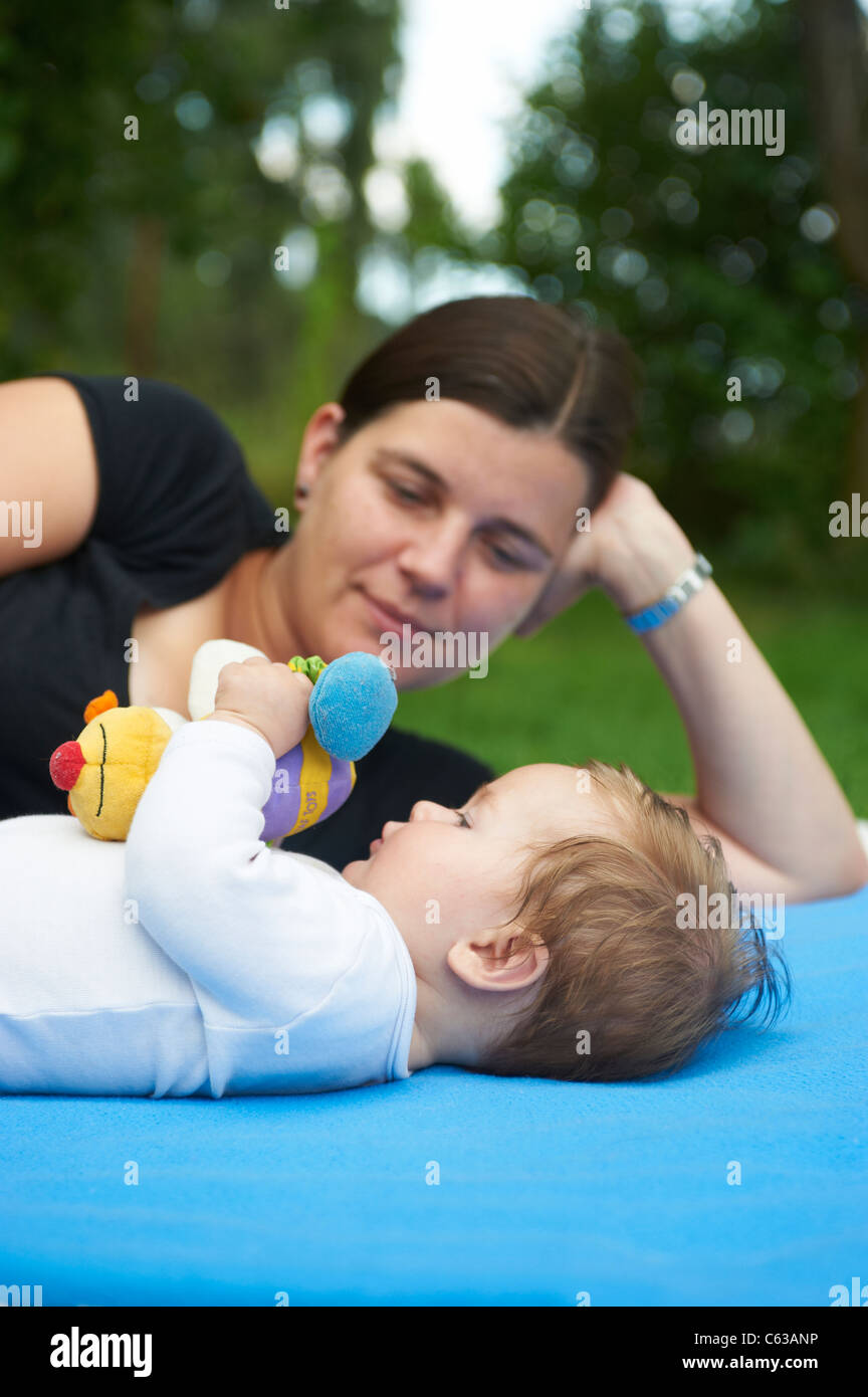kleines Kind Mädchen auf blaue Decke liegend mit Mutter im grünen Rasen außerhalb Stockfoto