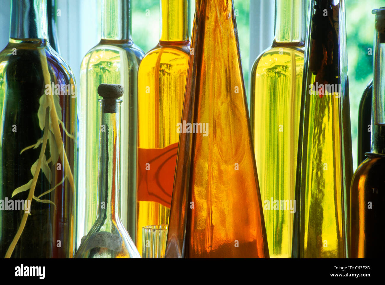 Flaschen in verschiedenen Formen und Farben gefüllt mit Essig, Öle und gewürzte Flüssigkeiten sitzt auf der Fensterbank im reflektierten Sonnenlicht Stockfoto