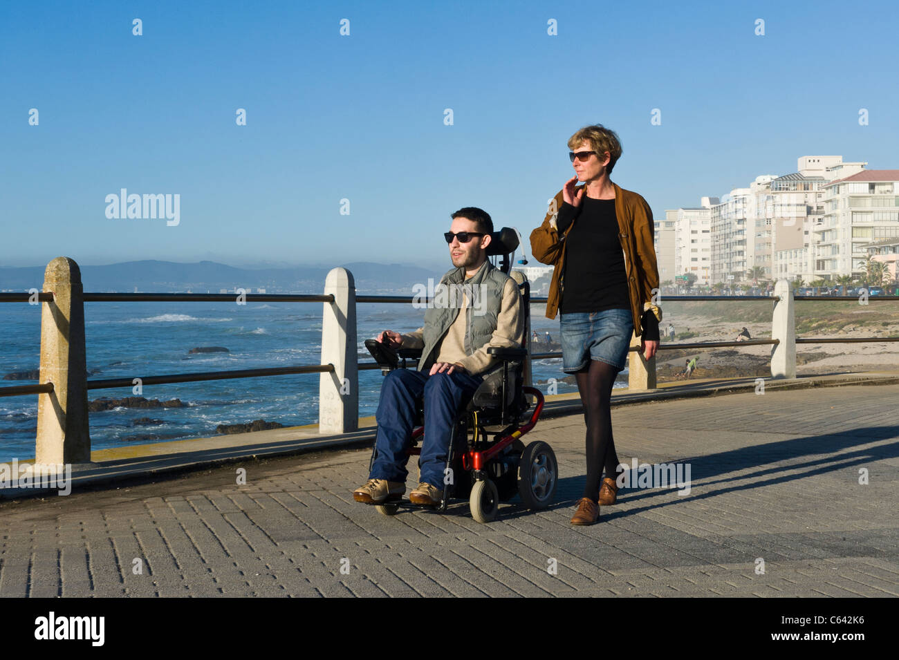Person in einem Rollstuhl mit Betreuer genießen Sie einen Ausflug an der Beach Road in Cape Town, South Africa Stockfoto