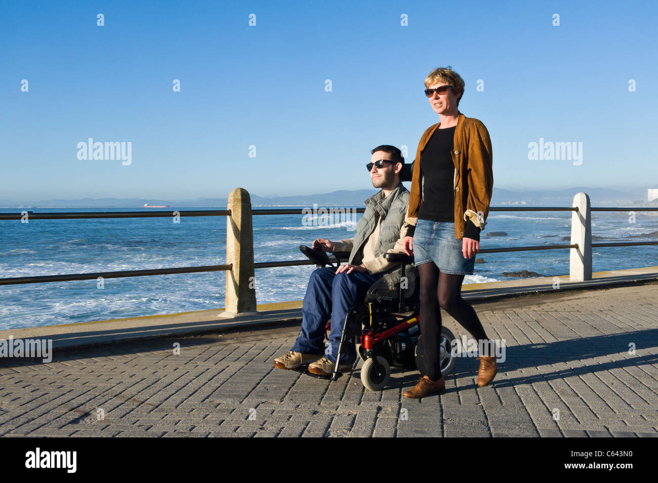 Person in einem Rollstuhl mit Betreuer genießen Sie einen Ausflug an der Beach Road in Cape Town, South Africa Stockfoto