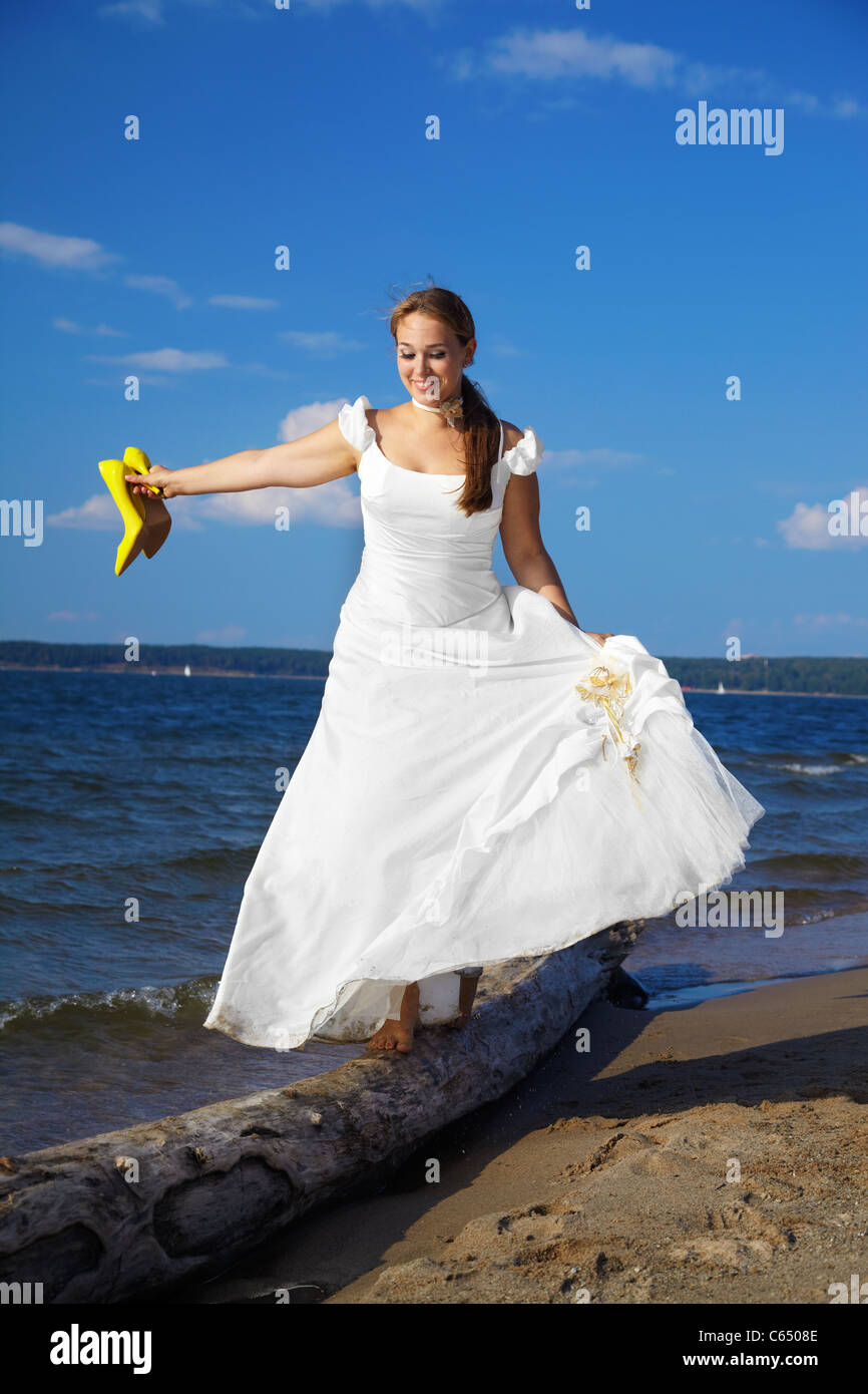 schöne slawische Braut am Ufer des Meeres balancieren auf Stamm mit gelben Pumps in den Händen Stockfoto