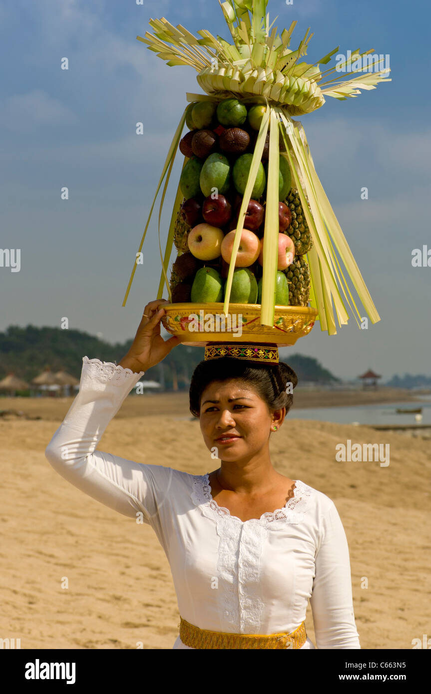 Balinesin in traditioneller Tracht, die am Strand mit Obstkorb oder Canang Sari auf dem Kopf herumläuft. Stockfoto