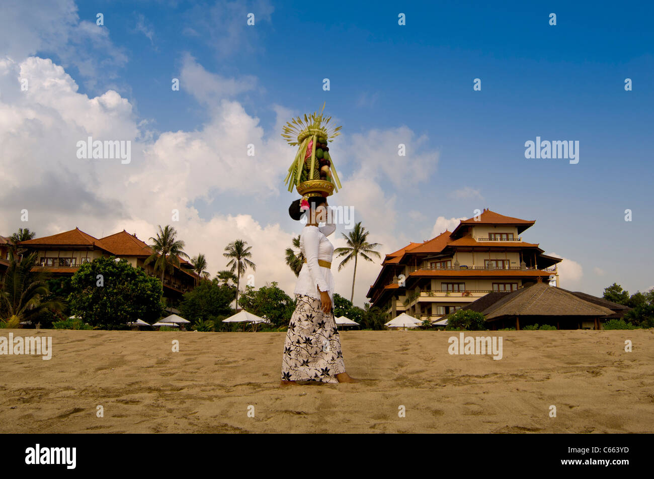 Balinesin in traditioneller Tracht, die am Strand mit einem Obstkorb oder Canang Sari auf dem Kopf herumläuft. Stockfoto