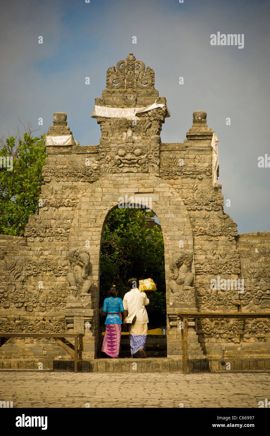 Balinesischer Mann und Frau, die einen Tempel betreten, tragen einen Korb mit religiösen Gaben. Stockfoto
