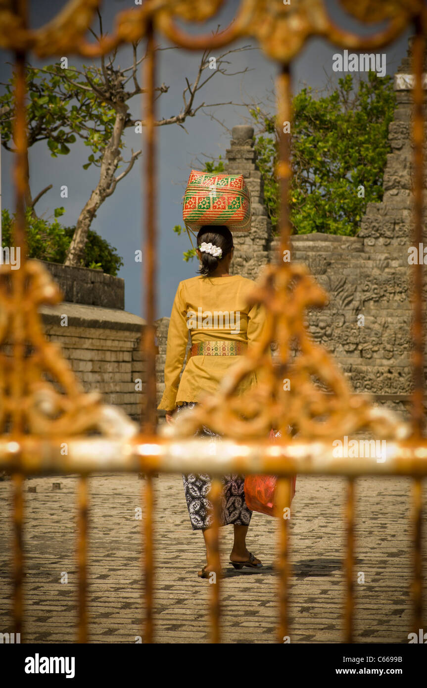 Rückansicht des balinesischen Frau, die religiöse Angebote zum Tempel in Korb auf dem Kopf trägt. Durch Tempel Tor geschossen. Stockfoto