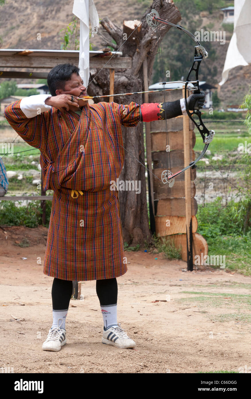 Mann in traditioneller Gho einen Bogen zu schießen. Paro Bogenschießen Boden. Bhutan Stockfoto