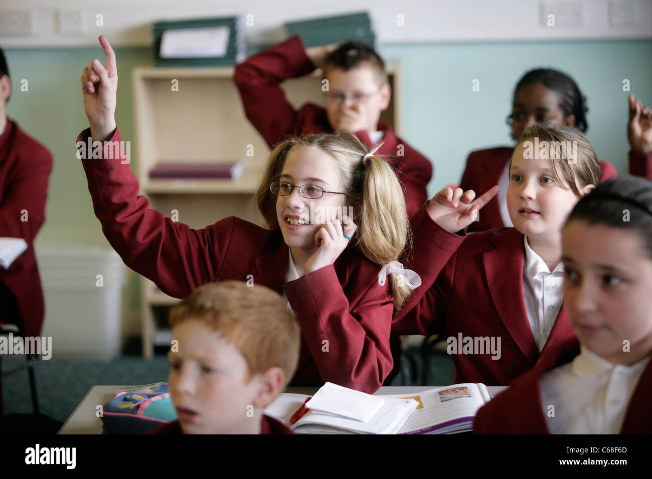 Ein Schüler an einer Sekundarschule in Großbritannien legt ihre Hand während einer Unterrichtsstunde eine Frage beantworten. Stockfoto