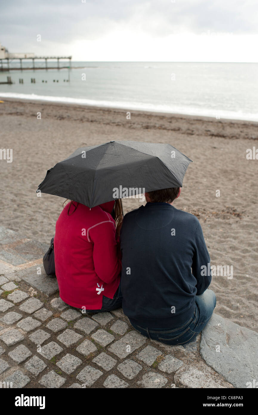 Ein paar im Urlaub bergende unter einem Regenschirm im Regen, august Sommernachmittag, Aberystwyth Wales UK Stockfoto