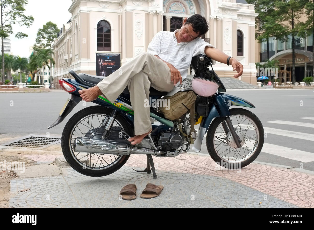 Eine vietnamesische Herr nimmt ein Nickerchen auf seinem Moped in der Nähe von Stadttheater in Ho-Chi-Minh-Stadt, Vietnam Stockfoto