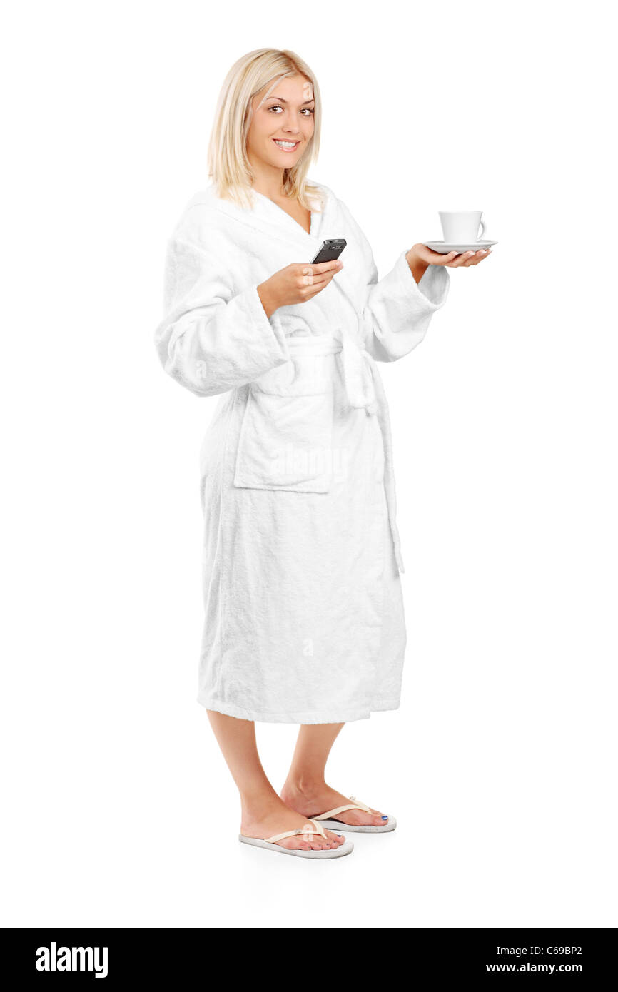 Voller Länge Porträt einer jungen Frau im Bademantel hält eine Kaffeetasse und Handy Stockfoto
