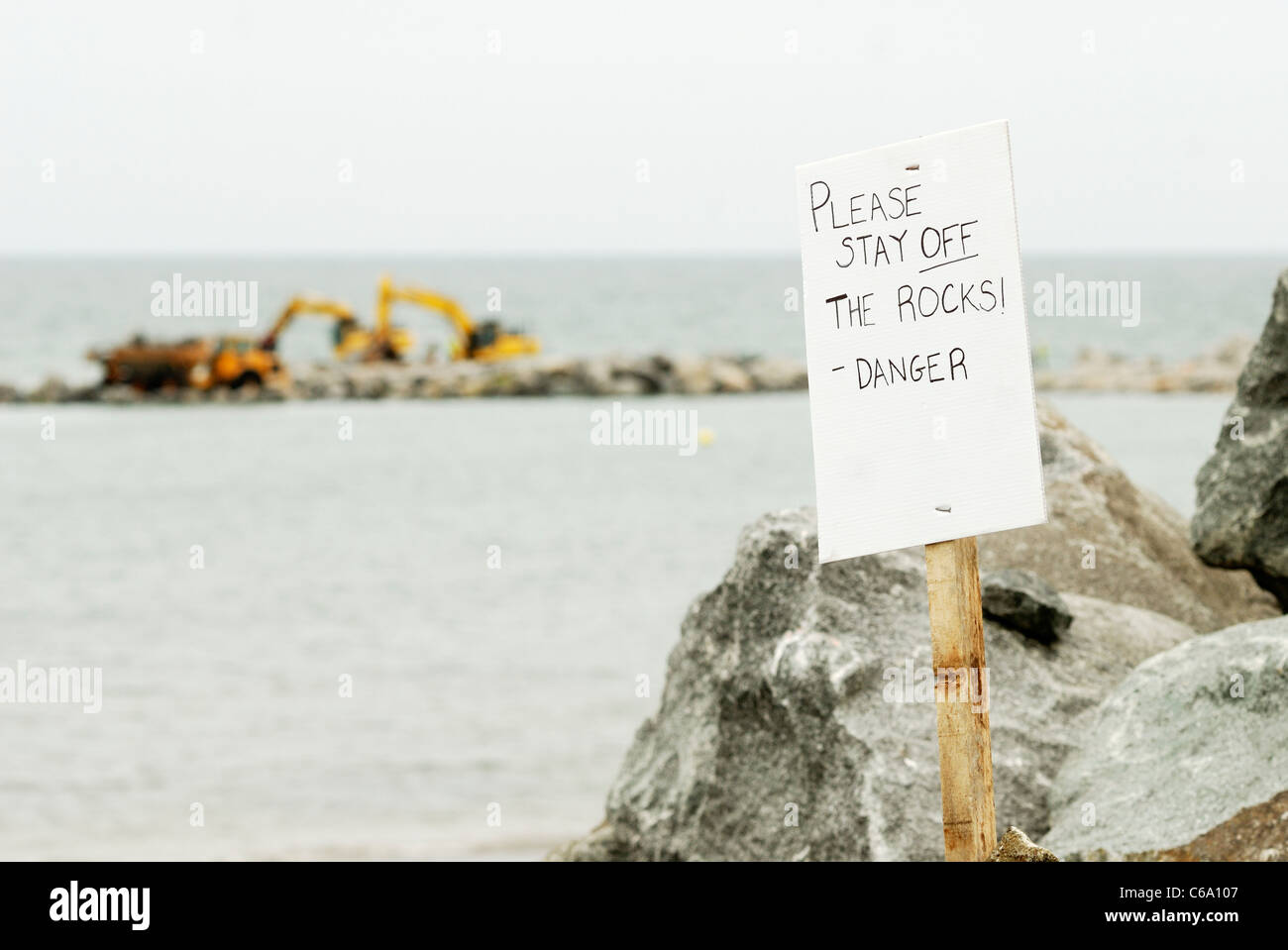 Unterzeichnen Sie auf einer Baustelle der Meer Verteidigung, Borth, Ceredigion, Wales lesen "Bitte bleiben Sie von den Felsen - Gefahr" Stockfoto