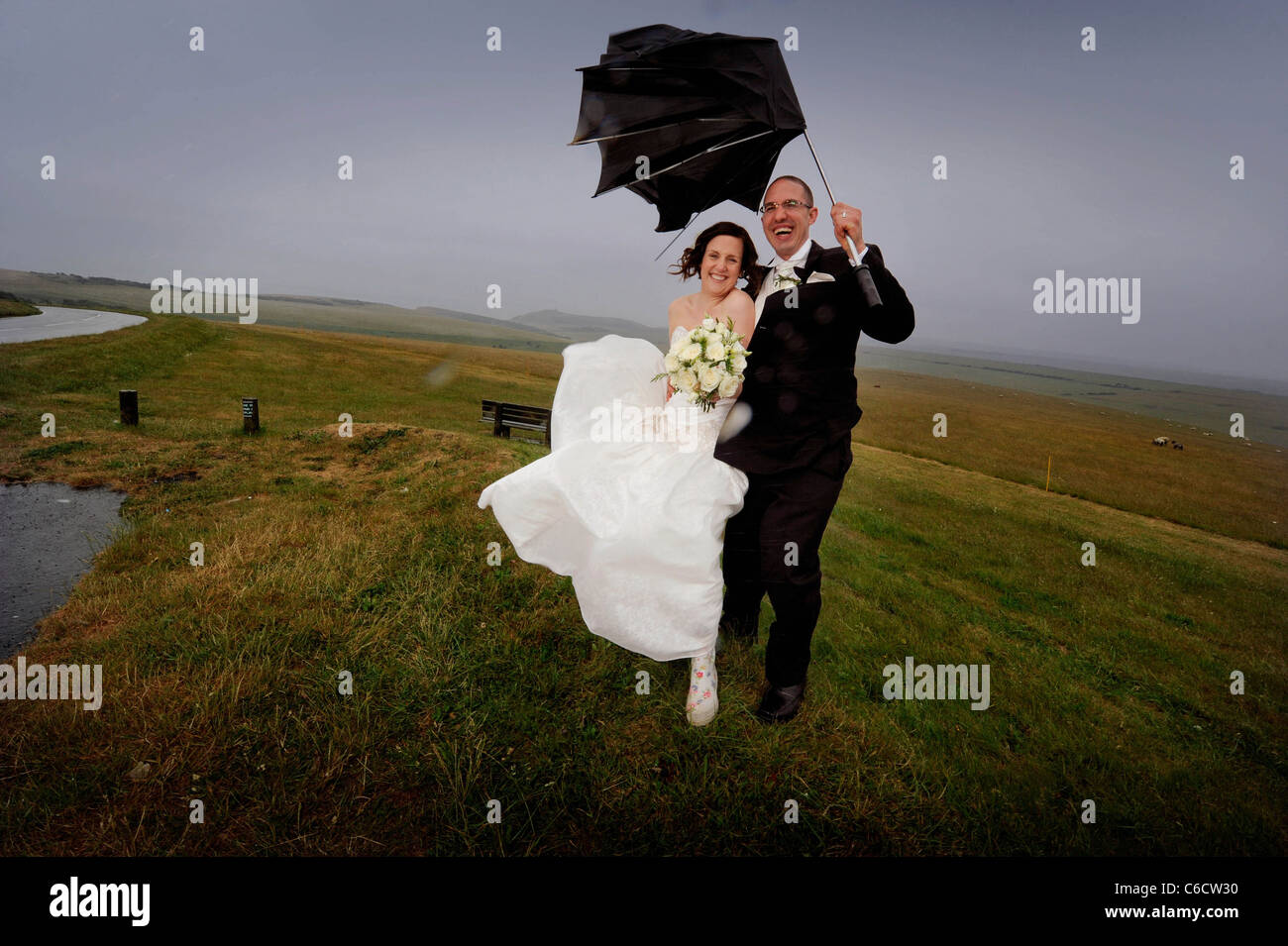 Der strömende Regen dämpft die Hochzeit des glücklichen Paares Sandra und Scott nicht, da sie bei starkem Wind auf Beachy Head posieren. Stockfoto