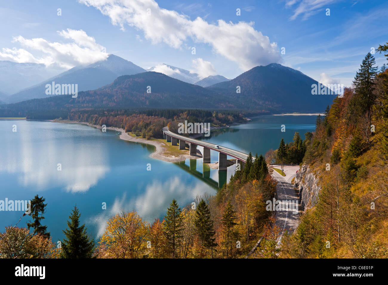 Reflexionen einer Straße Brücke über See Sylvensteinspeicher, mit Bergen im Hintergrund, in Bayern, Deutschland Stockfoto