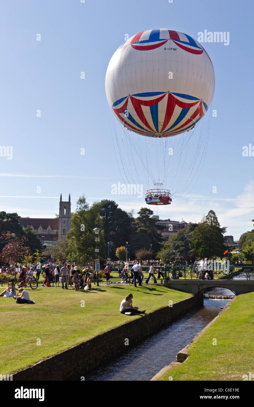 Bournemouth Eye Helium Beobachtung Ballon an schönen sonnigen Tag mit Menschen entspannen im Garten neben fließenden Wasser Stockfoto