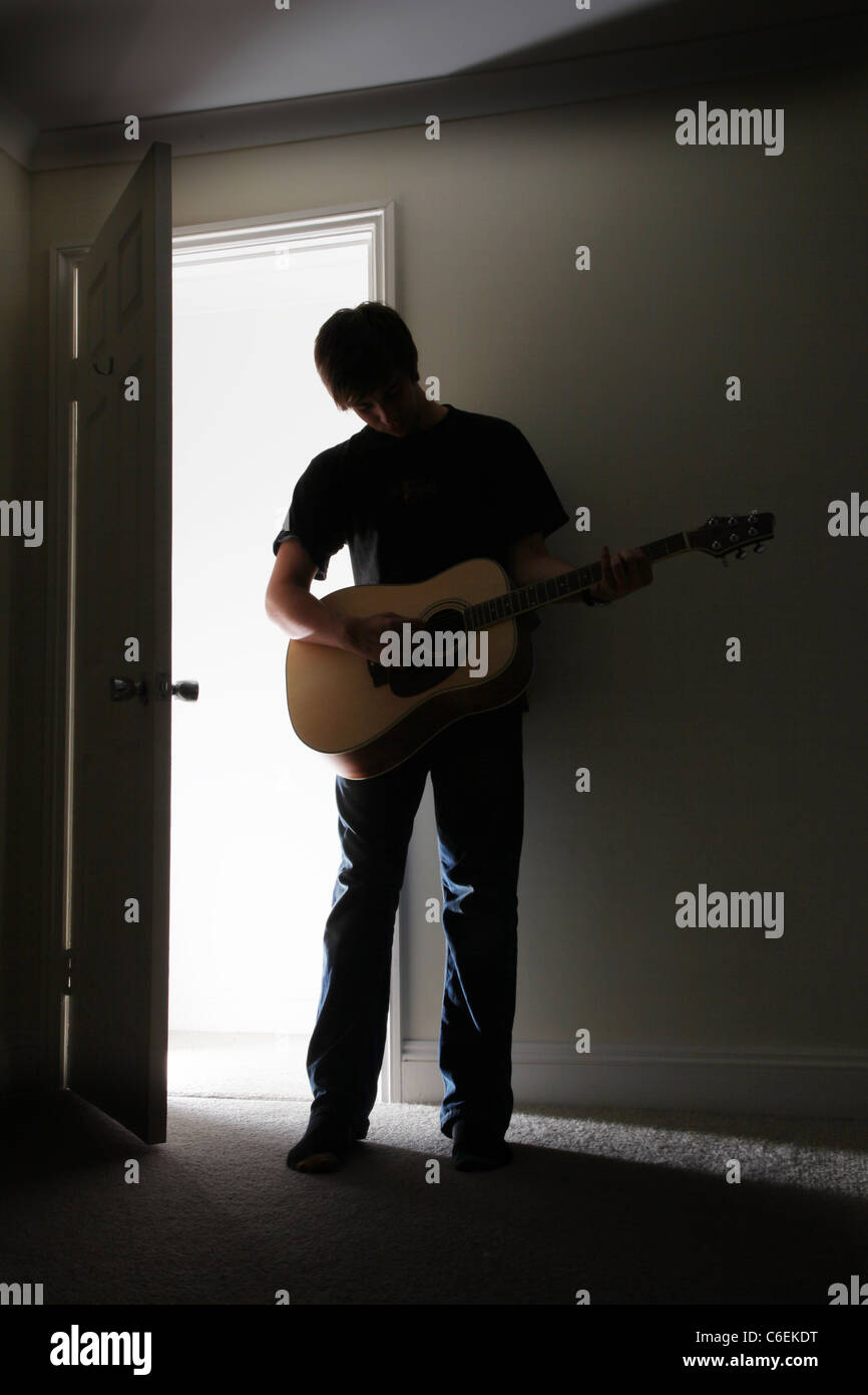 Junger Mann stehend in einem dunklen Raum eine akustische Gitarre zu spielen. Stockfoto