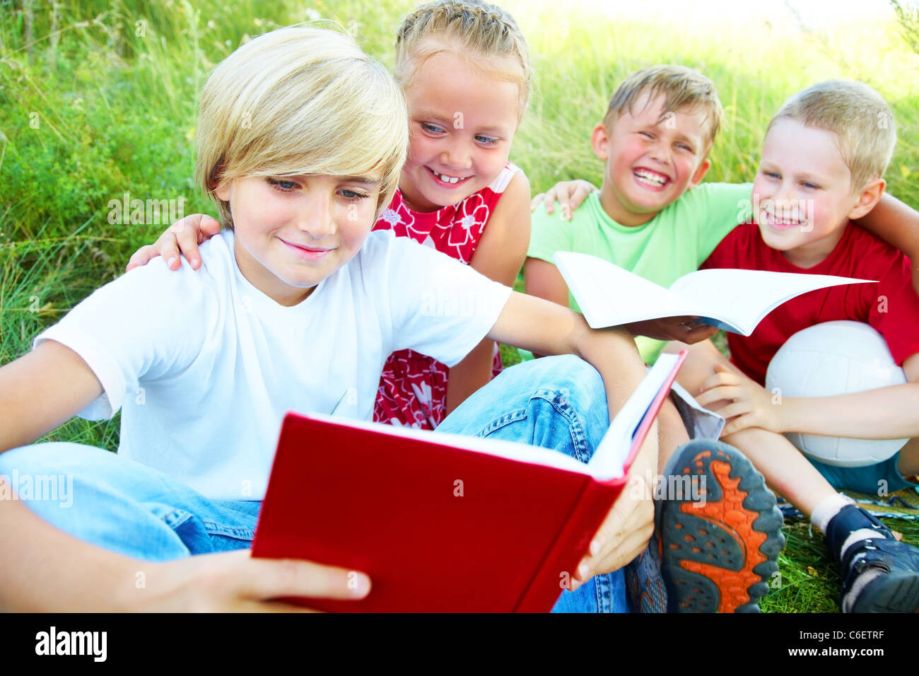 Grundschulkinder, die das gleiche Buch lesen, in der späten Nachmittagssonne genießen Stockfoto